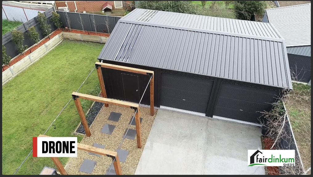 Aerial view of a dark-roofed shed, driveway, and lawn, with Drone and Fair Dinkum Sheds labels.