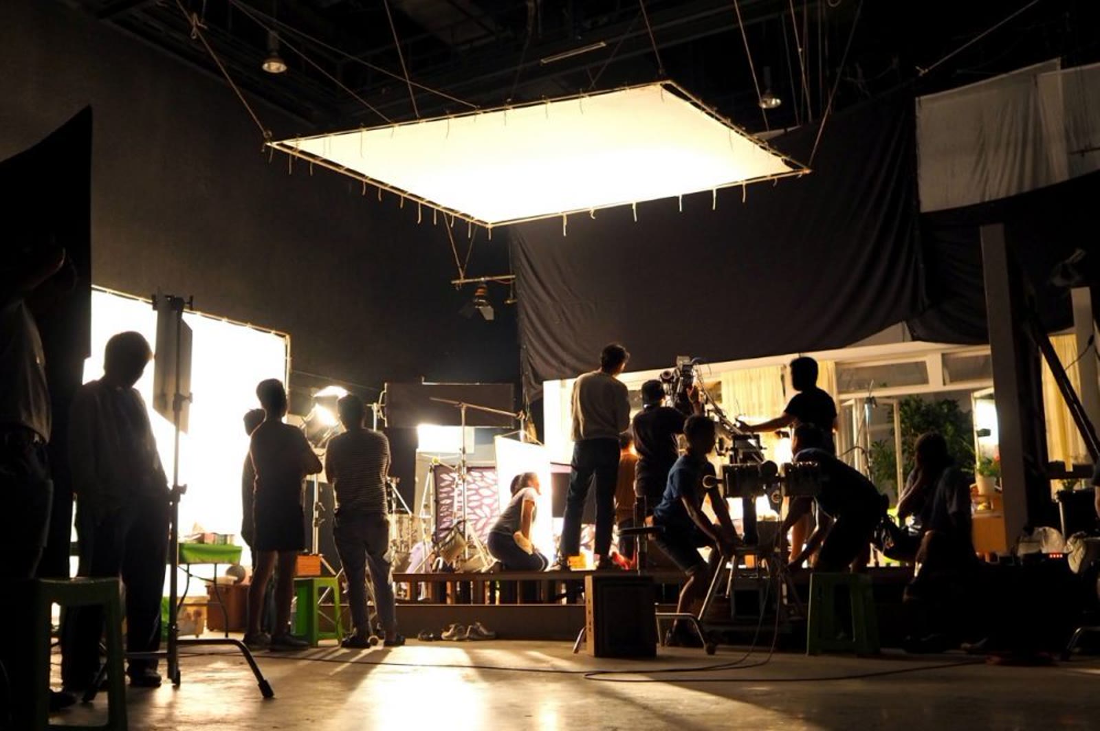 Camera operator and boom operator filming a woman in a studio.
